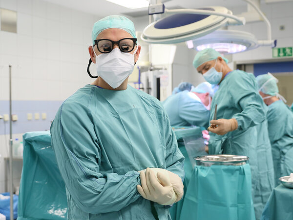 Blick in einen OP - im Vordergrund Dr.  Steffan Jackobs in grüner OP-Kleidung mit Mundschutz, OP-Brille und Haube