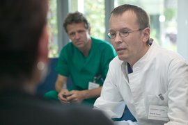 Prof. Dr. Peter Tonner und Thomas Kavermann in Dienstkleidung von vorne im Gespräch mit einem älteren Patienten (von hinten)