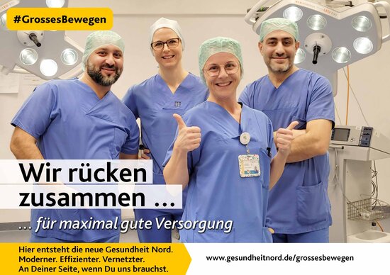 Vier OP-Pflegekräfte in blauer Dienstkleidung vor eine OP-Lampe. Im  Vordergrund hält eine Pflegekraft beide Daumen nach oben.