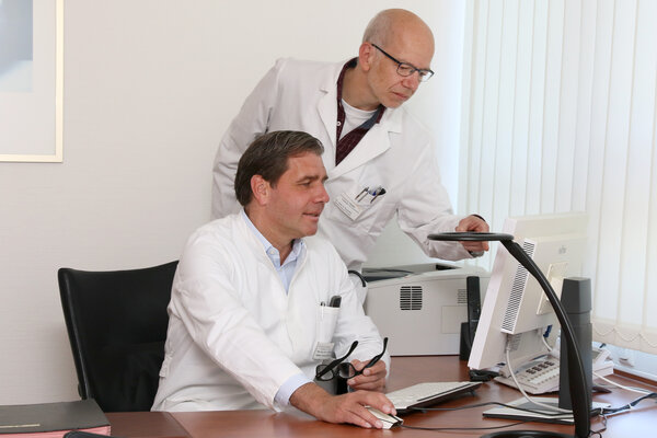 Priv.-Doz. Dr. Arnd-Steffen Böhle und Dr. Dietmar Ruschke in weißer Dienstkleidung im Büro vor einem Monitor