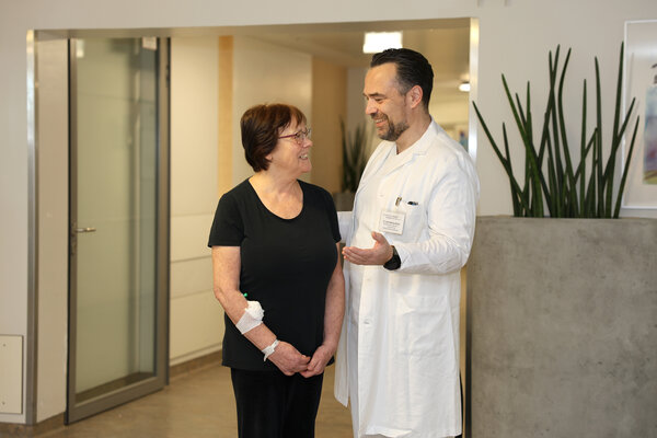 Dr. Matthias Müller im weißen Kittel auf einem Krankenhausflur im Aufklärungsgspräch mit einer Patienten