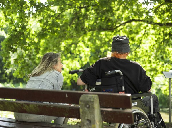 Junge Frau und Rollstuhlfahrer ruhen sich bei einer Bank im Park aus