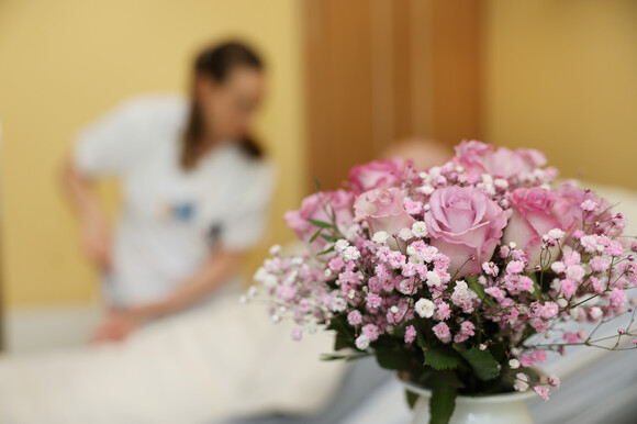 Pflegekraft im Patientenzimmer - im Vordergrund ein frischer Blumenstrauß