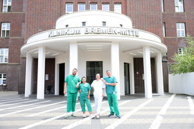 Vier Mitarbeitende in Klinikkleidung vor dem heutigen Haupteingang des Klinikums Bremen-Mitte