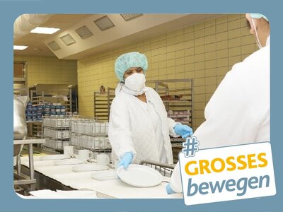 Zwei Küchenarbeiter in weißer Schutzkleidung am Portionierband
