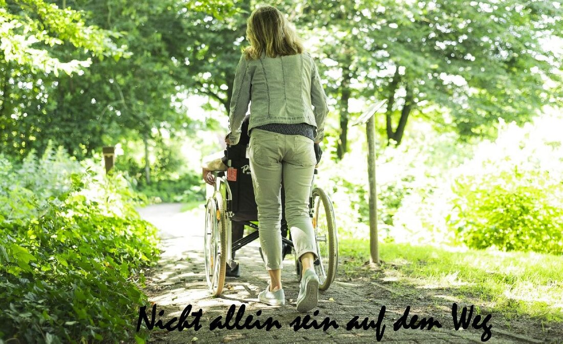 Eine Frau schiebt einen Rollstuhlfahrer durch einen Waldweg - eingedruckt ist der Text "Nicht allein sein auf dem weg"
